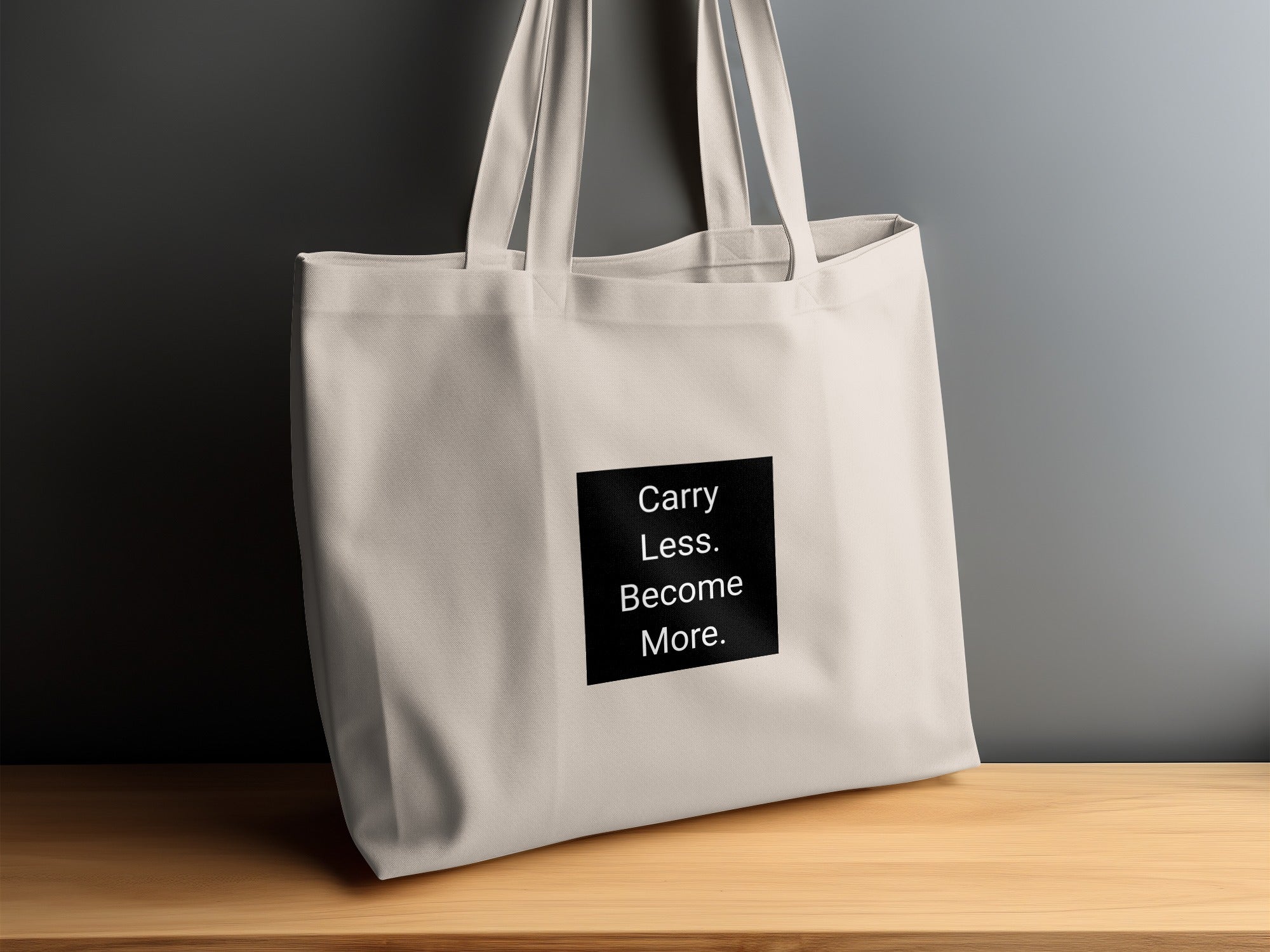 Light beige tote bag with black square text: "Carry Less. Become More."