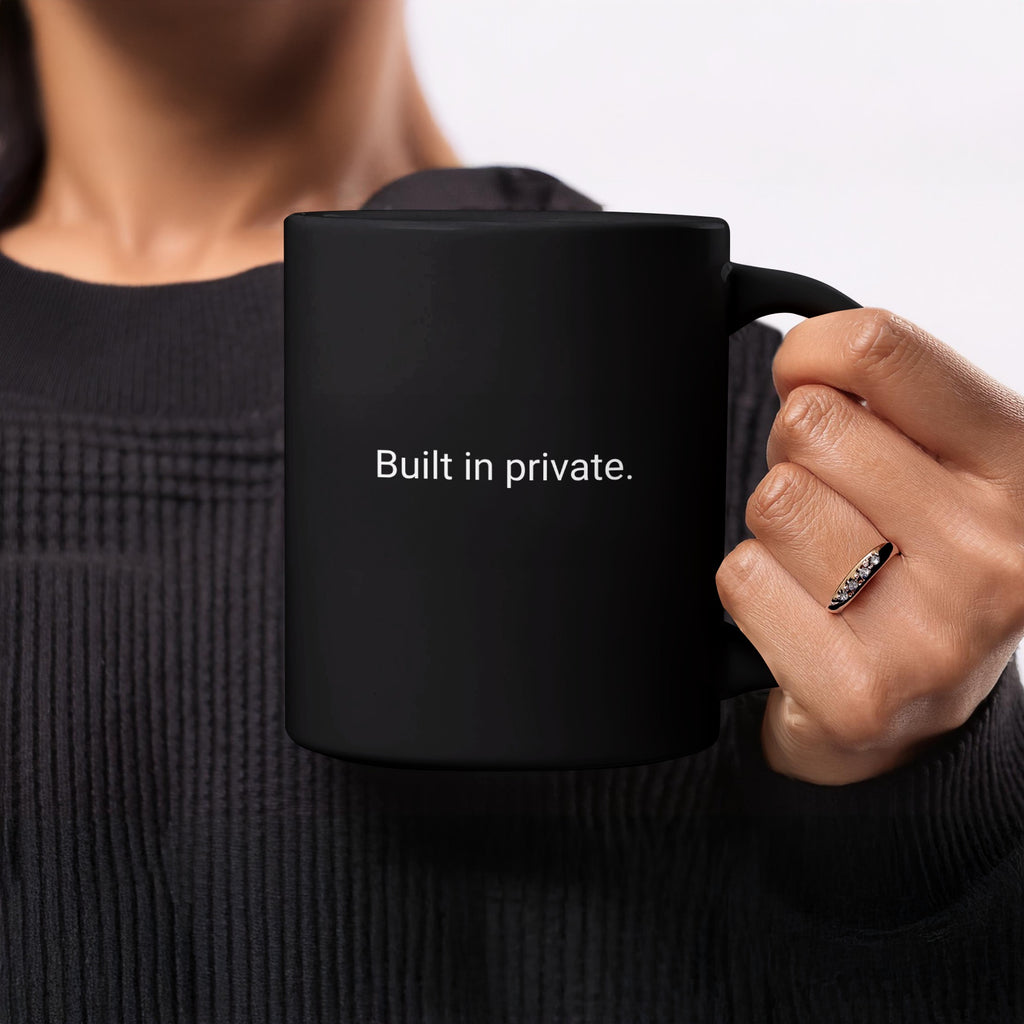 Black mug with white text "Built in private." held by a person.