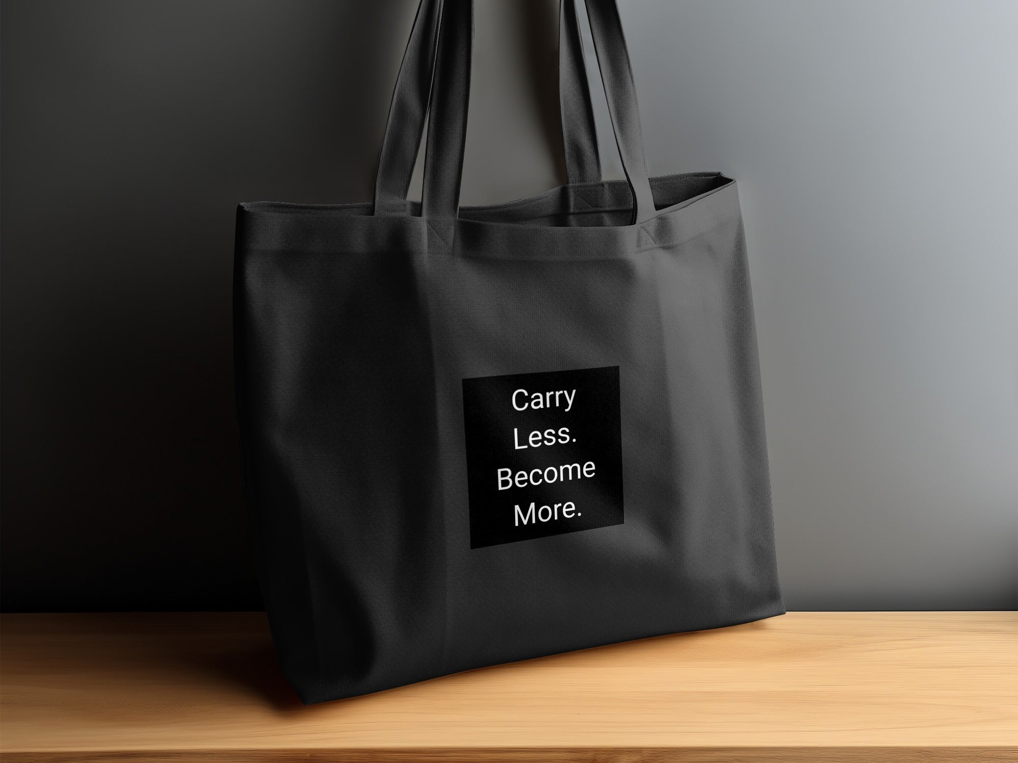 Black tote bag with white text: "Carry Less. Become More."