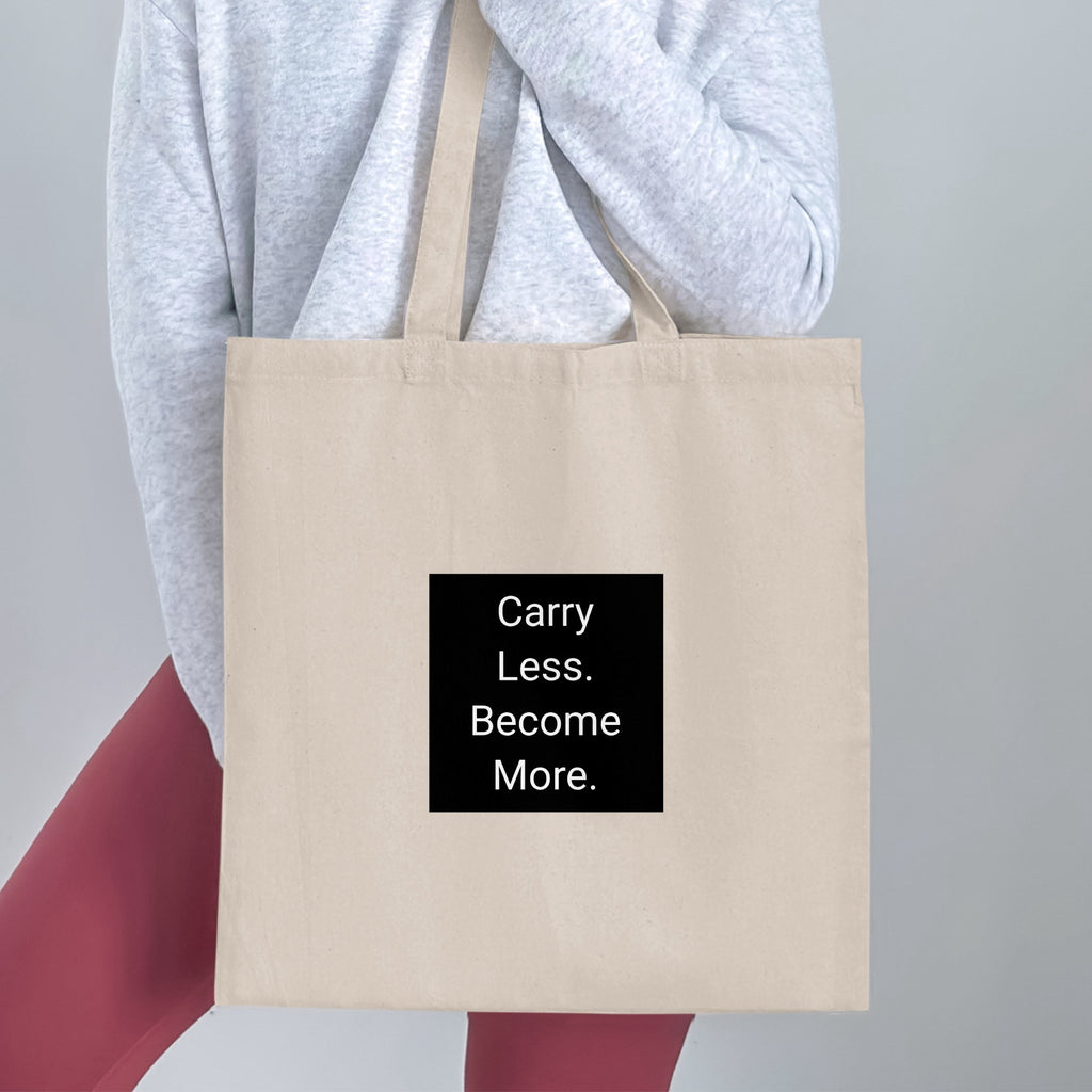 Tote bag with "Carry Less. Become More." text on a black square.