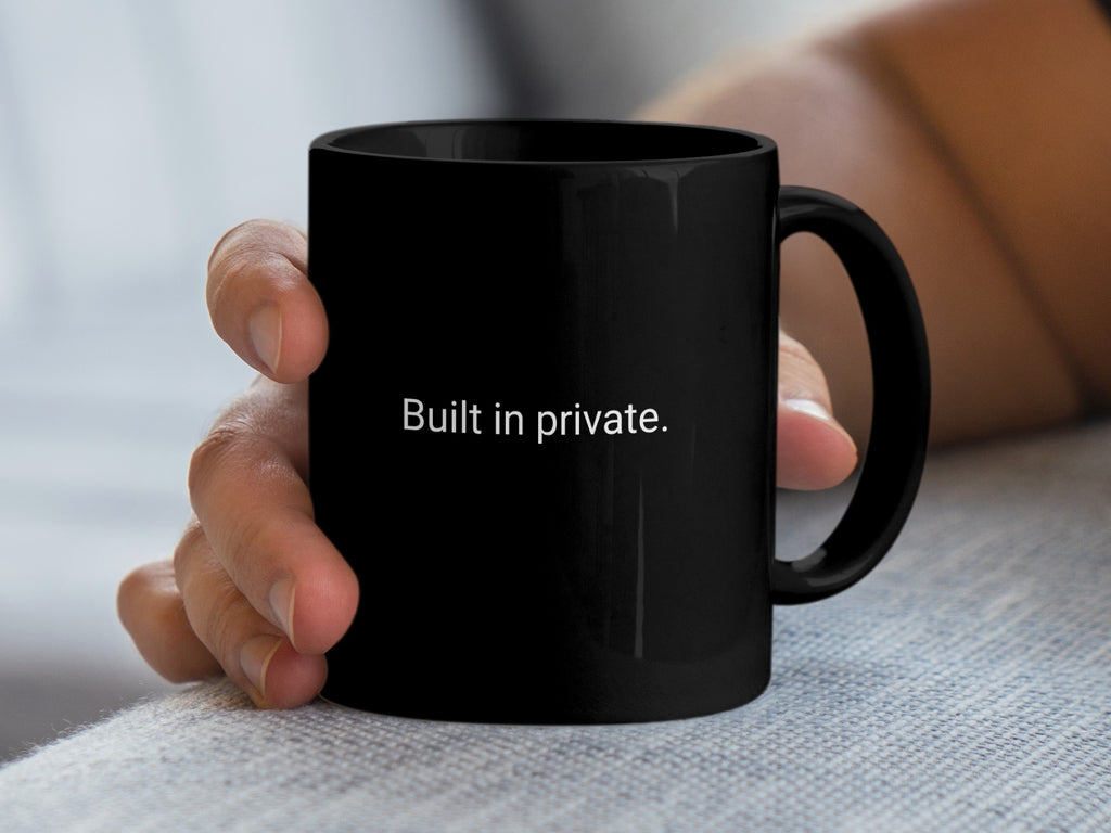 Black mug with white text "Built in private." held by a hand.