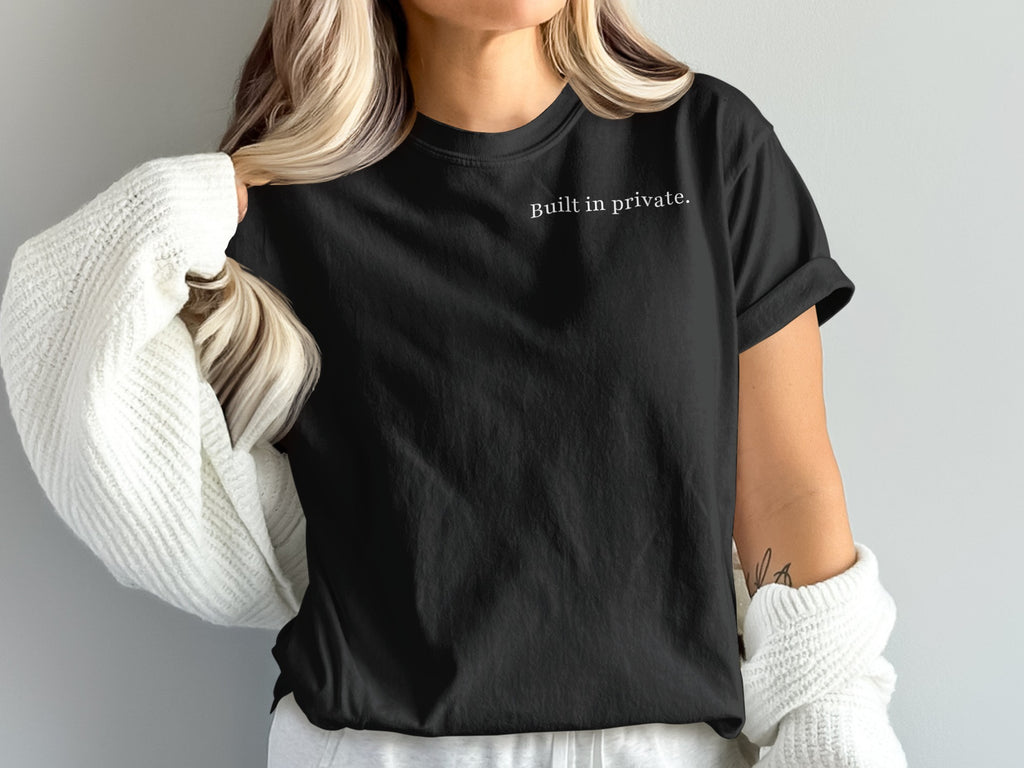 Black t-shirt with "Built in private." text, worn by a person with a white sweater.